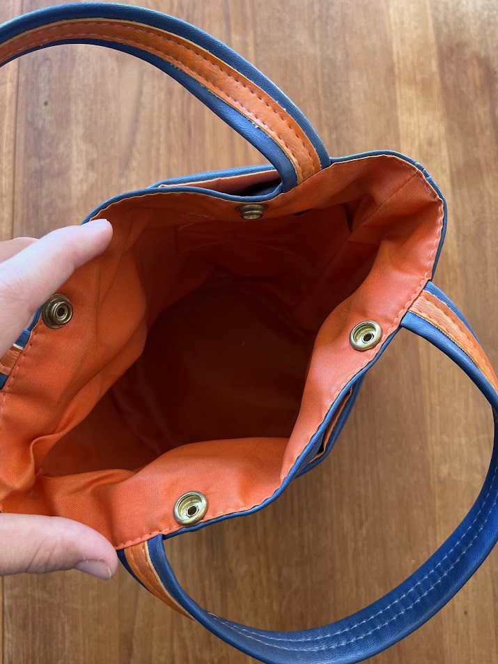 Blue vinyl Gators purse open showing orange lining and brass snaps