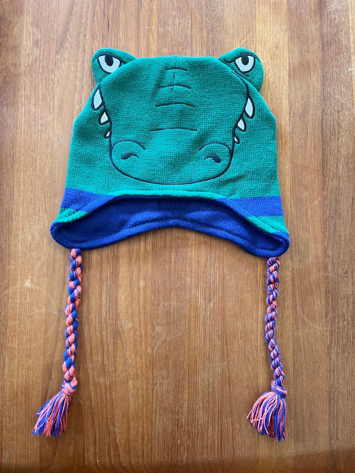 Gators mascot knit hat laid flat showing gator face, ear flaps and braided tassels